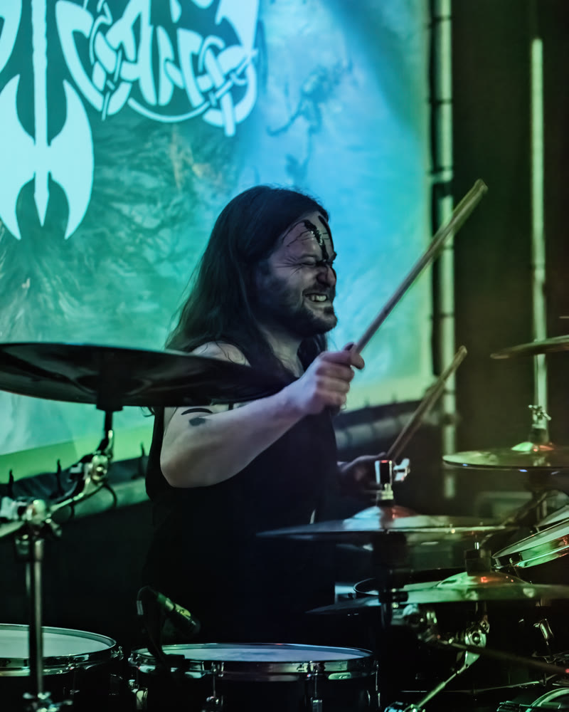Sebi behind the drum kit, face paint on, in front of the band banner