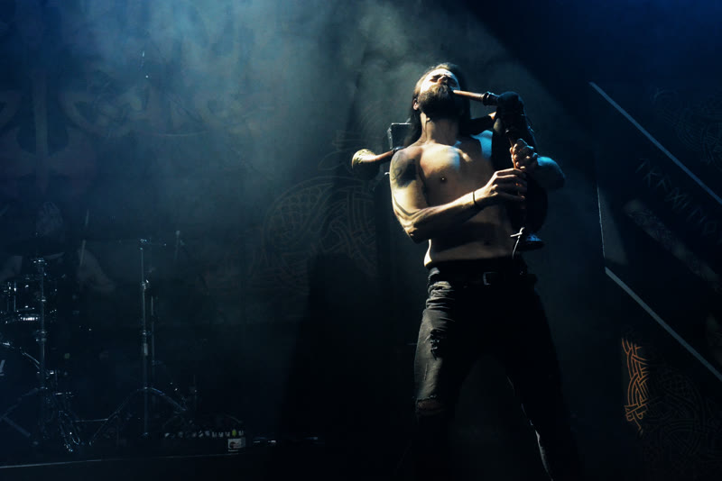 Muscus playing the bagpipes in backlight, in front of the Dvalin banner